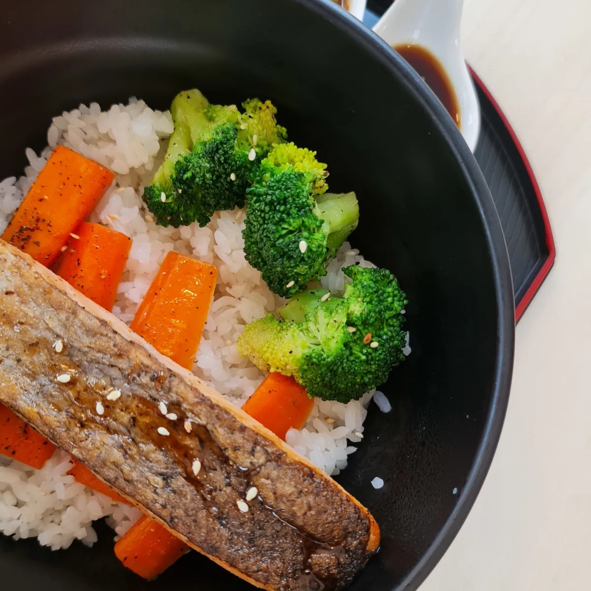 Seared salmon over fluffy white rice with bright orange carrots and green broccoli in a black bowl